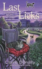 Cover for Last Licks by Claire Donally. In the background is a grand mansion, complete with fountain and hedge maze. A cat walks up the garden path. In the foreground is a wheelchair with a red cushion, on which sits a cat cleaning its paw.