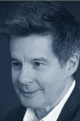 A b&w headshot of Donald Maass - smiling gently. He is wearing a white collared oxford and dark suit jacket.